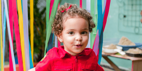 Menina de cabelo cacheado e blusa vermelha sorrindo em festa